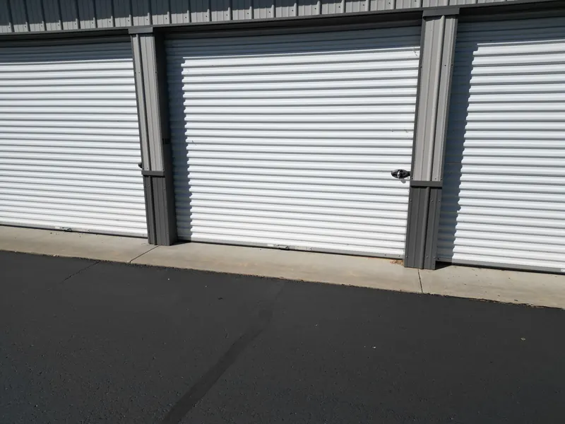 Close-up of a clean white roll-up storage unit door with its latch and a concrete apron below
